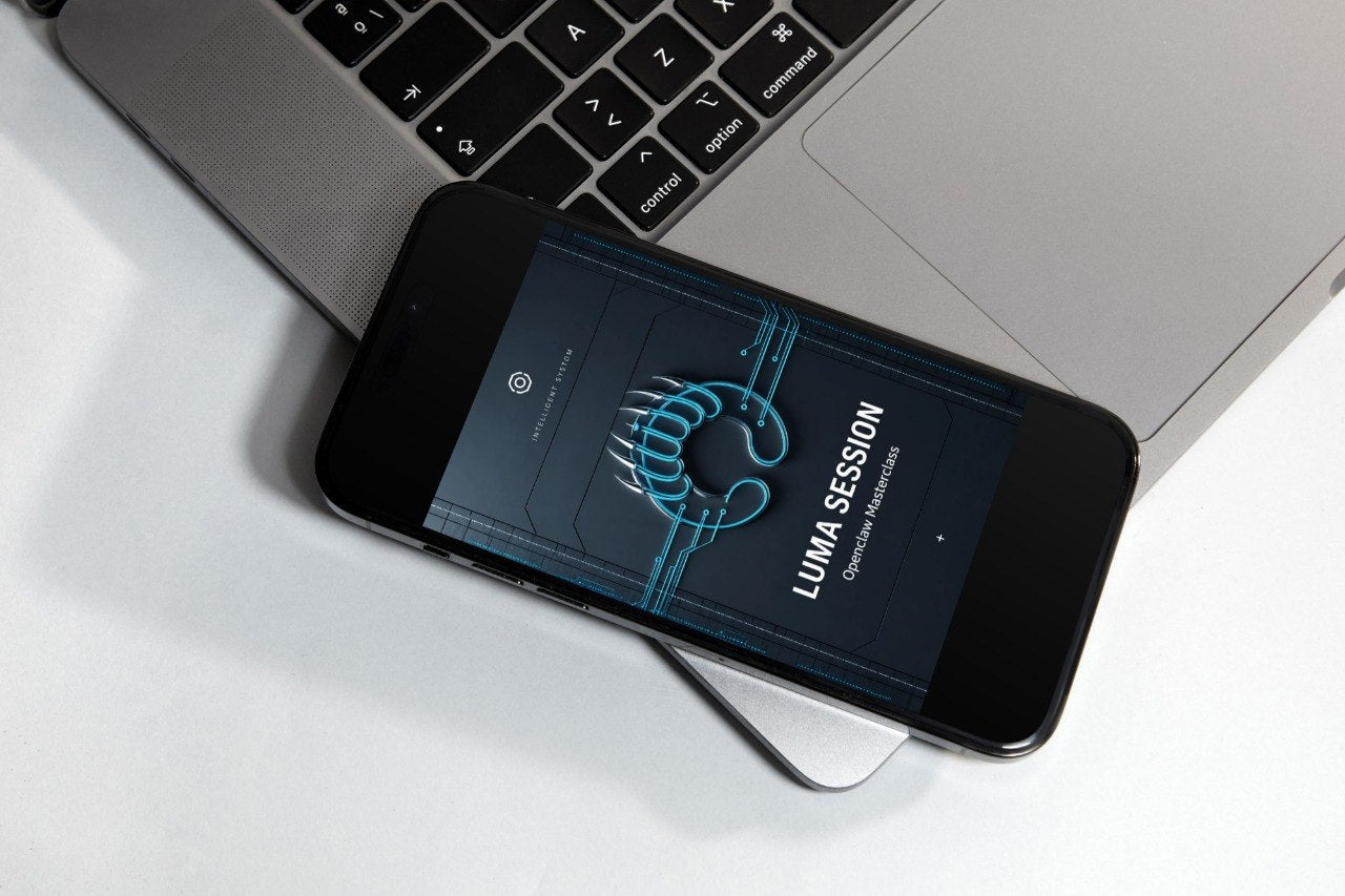 A smartphone on a small display stand showing the 'LUMA SESSION' logo on its screen, set against a dark gray textured background.