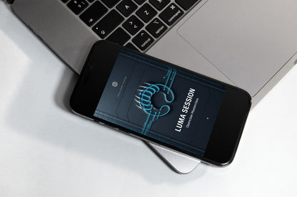 A smartphone on a small display stand showing the 'LUMA SESSION' logo on its screen, set against a dark gray textured background.
