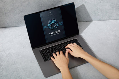 A dark gray laptop sits open on a light gray tabletop against a textured gray wall. The screen displays a digital cover titled 'TIER SESSION' with orange graphic accents.